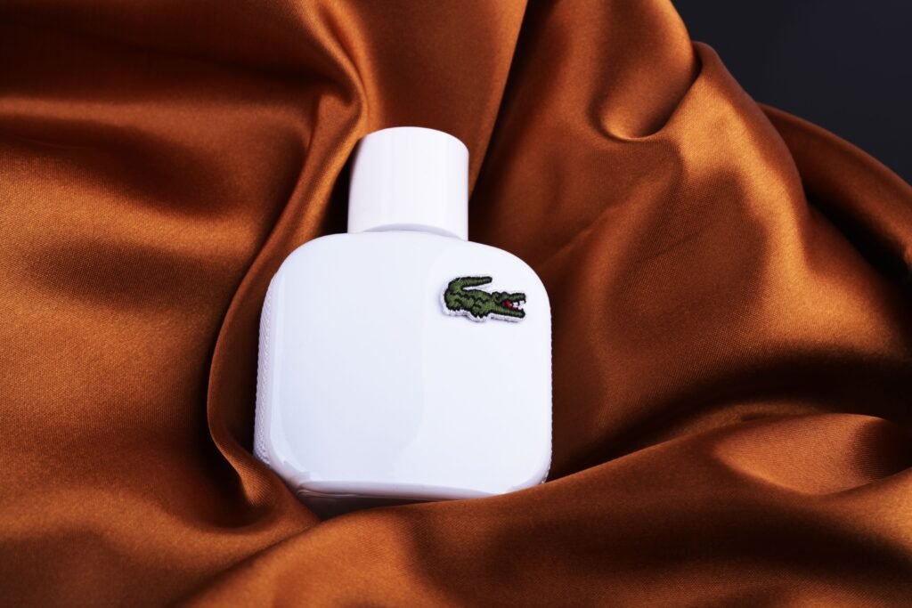 White perfume bottle with crocodile logo resting on rich brown silk, showcasing elegance and sophistication.